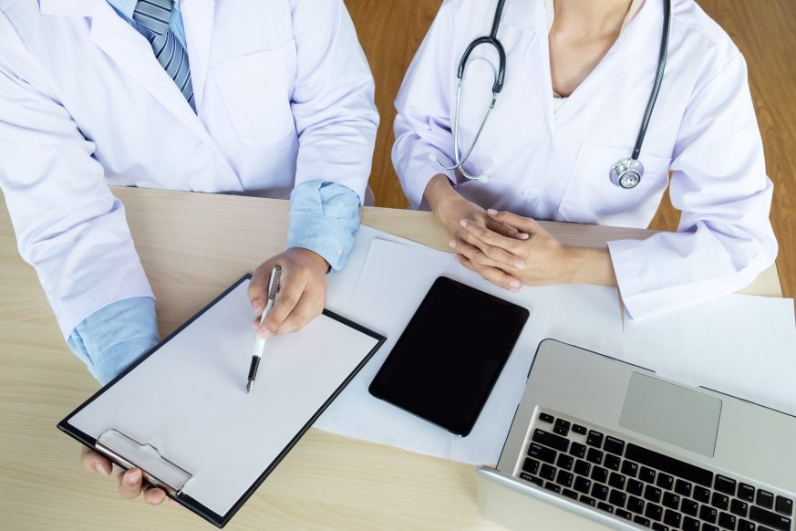 doctors looking over clipboard with tablet and laptop