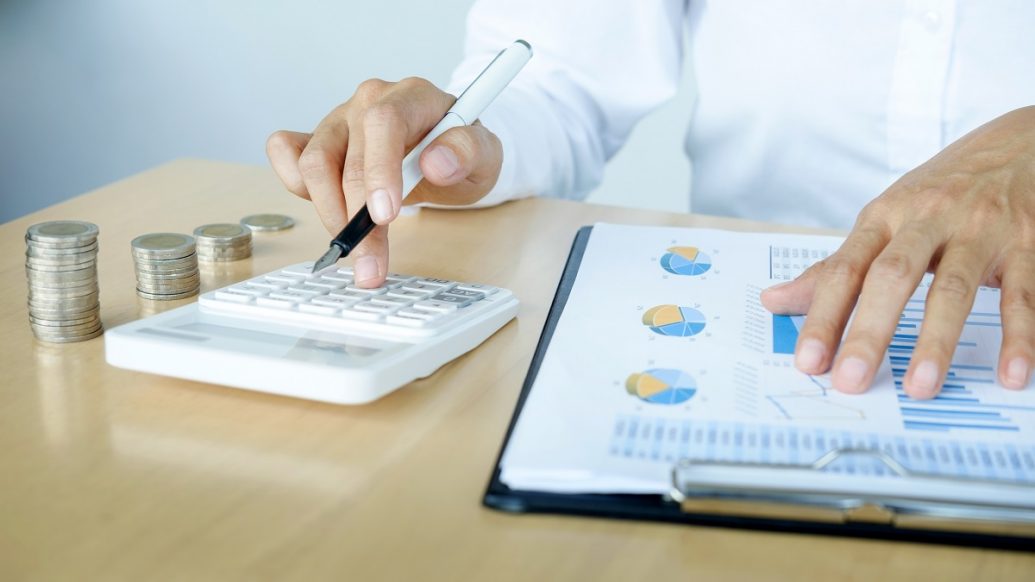 person looking over money documents with calculator and fountain pen, with coins beside them