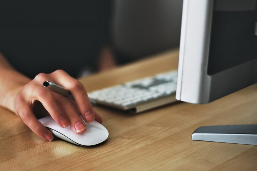 person working at mac computer holding mouse and stylus