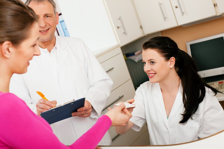 patient talking with receptionist with doctor looking on