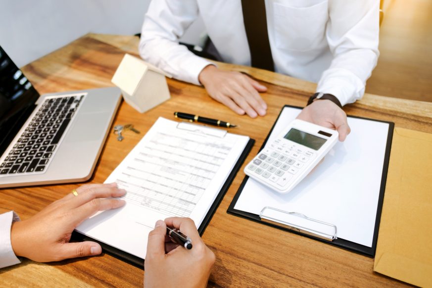 person signing document while another person is showing them numbers on their calculator