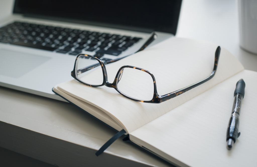 book with pen and glasses on it, with a laptop in the background